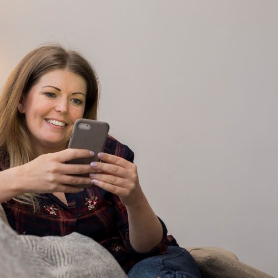 Woman sits on couch using her phone to pay rent